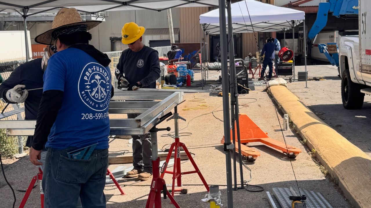 The crew in blue Pro-fusion shirts working under canopies on a lot, a lift and a pickup behind them.