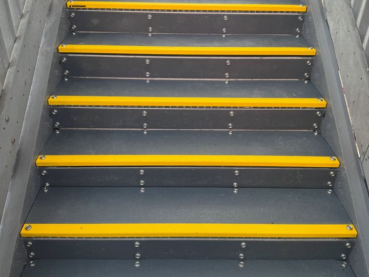 New grey steps with yellow nosing, rising between handrails.
