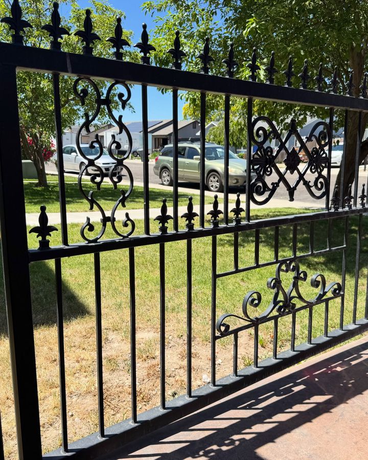 A black ornamental iron fence with scroll panels and spear-point finials along a front lawn.